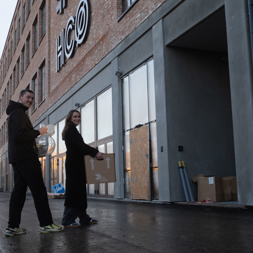 Studerende bærer laboratorieudstyr foran HCØ-bygningen på TEC – billede af studiemiljø og naturvidenskabelig undervisning