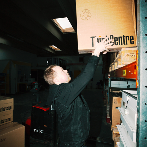 En lærling placerer en kasse på en hylde i lageret, lærling, lager, hylde, varerhåndtering, logistik, lagerarbejde