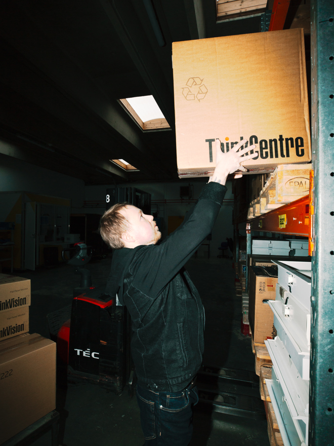 En lærling placerer en kasse på en hylde i lageret, lærling, lager, hylde, varerhåndtering, logistik, lagerarbejde