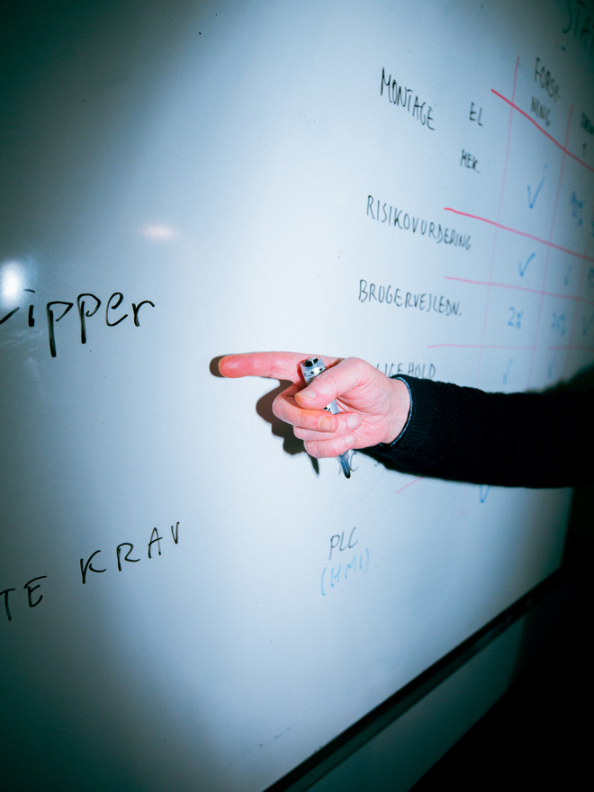 Underviser peger på en tavle med tekniske noter og diagrammer, præsentation, tavle, undervisning, teknik, planlægning