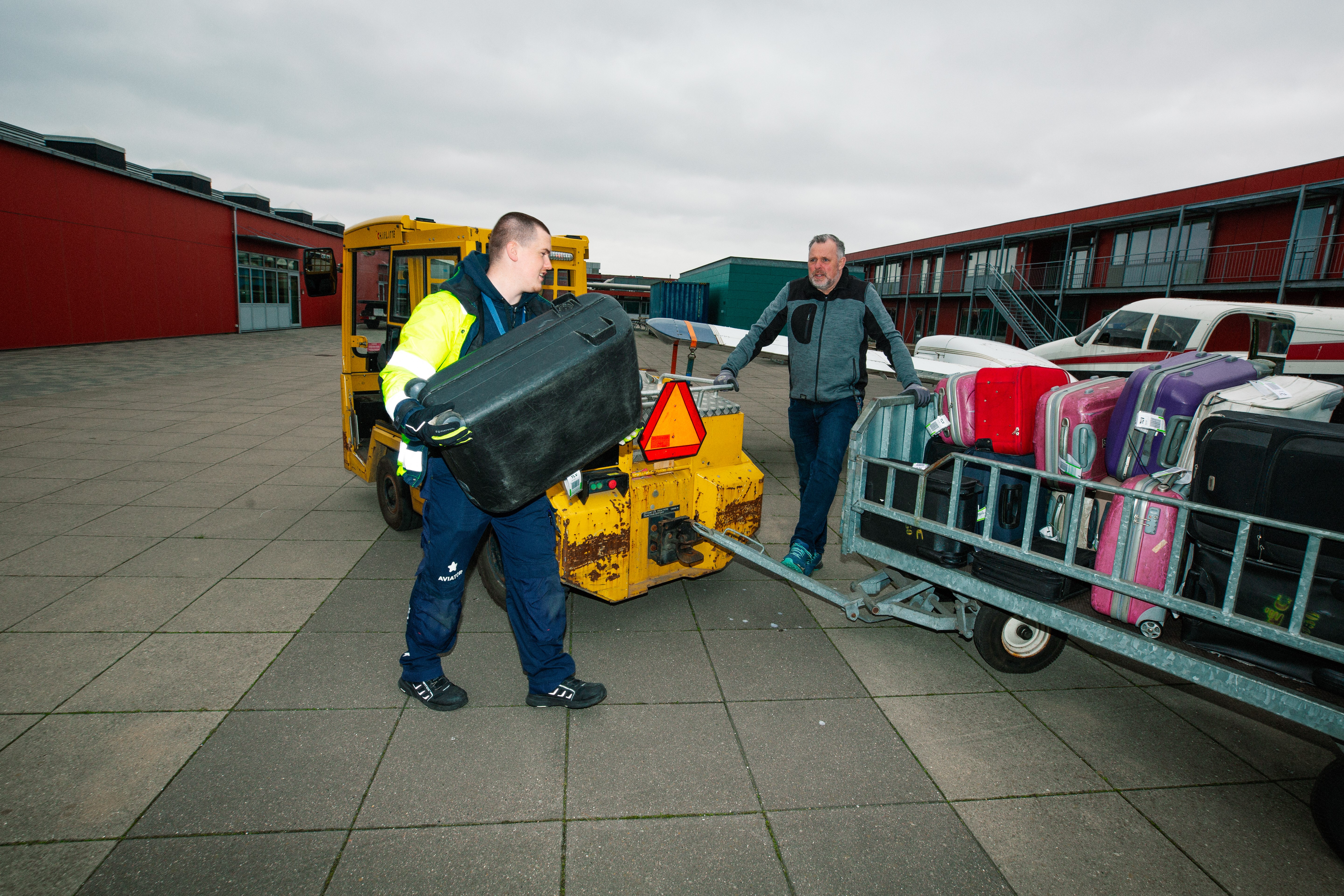 Lærling håndtere bagage, Bagagehåndtering, lufthavn, transport, sikkerhedsvest, udendørs arbejde, logistik, bagagevogn.