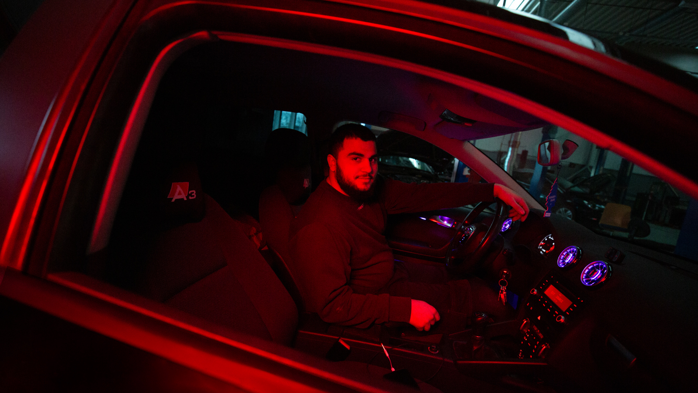 Person sidder i bil oplyst af rødt lys i et mørkt værksted, værksted, rødt lys, mekaniker, nat