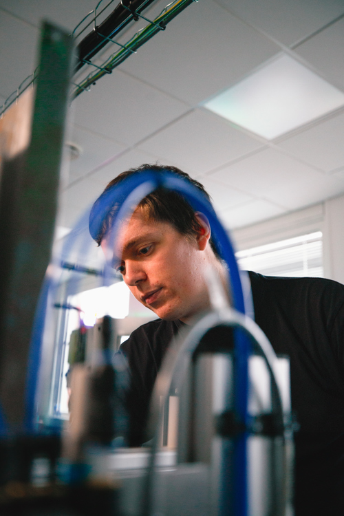 Elev fokuserer på arbejdet ved et maskineri med slanger og rør, maskinbetjening, automation, industri, teknik, arbejdsproces