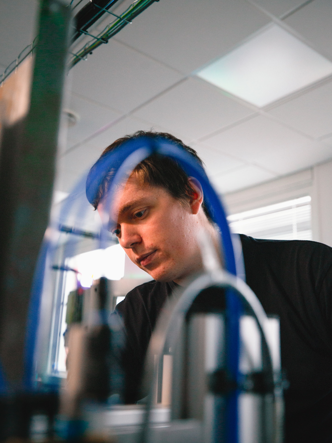 Elev fokuserer på arbejdet ved et maskineri med slanger og rør, maskinbetjening, automation, industri, teknik, arbejdsproces