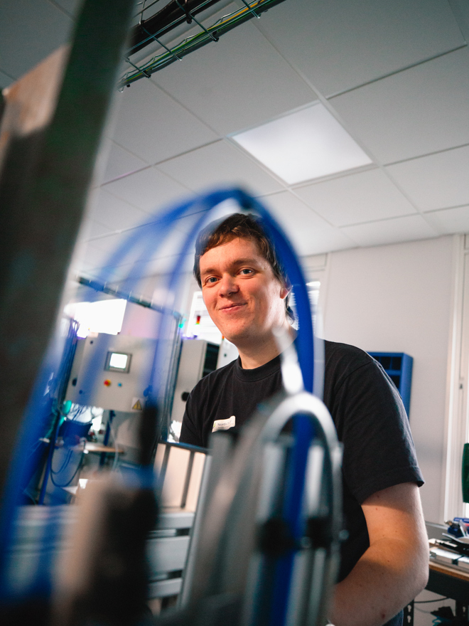 Elev smiler mens han arbejder ved et automatiseret system med slanger og maskiner, automation, maskinsystem, teknik, arbejde, industri