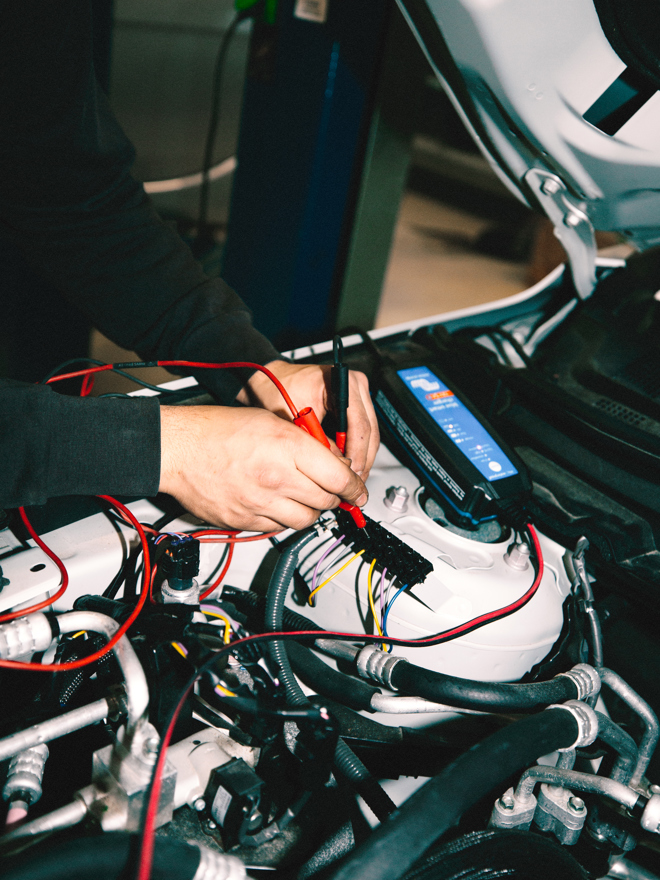 Mekaniker arbejder på ledninger i motorrummet under bilreparation, mekaniker, motorrum, ledninger, bilreparation, værksted