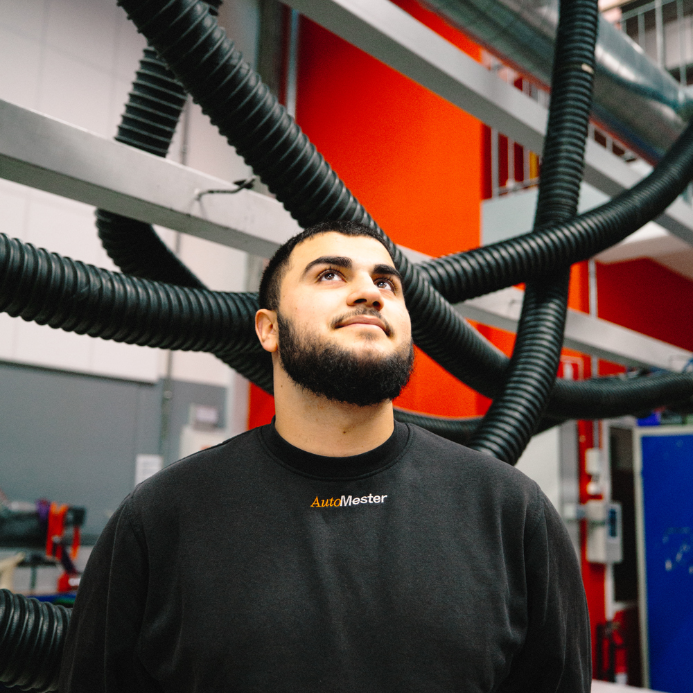 Mekaniker står under udsugningsrør i et værksted og kigger opad, mekaniker, værksted, udsugningsrør, arbejdsplads, portræt