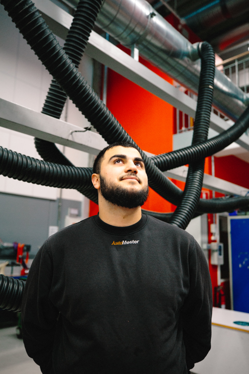 Mekaniker står under udsugningsrør i et værksted og kigger opad, mekaniker, værksted, udsugningsrør, arbejdsplads, portræt