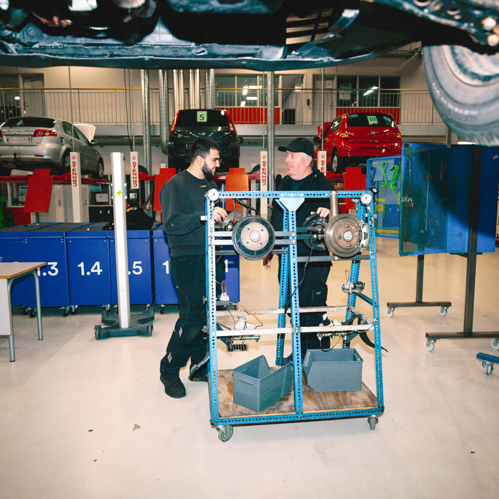 Lærling arbejder med værktøj på en løfteplatform i et værksted, lærling, værktøj, løfteplatform, personvognsmekaniker, værksted, mekanikeruddannelse, bilreparation, erhvervsskole.