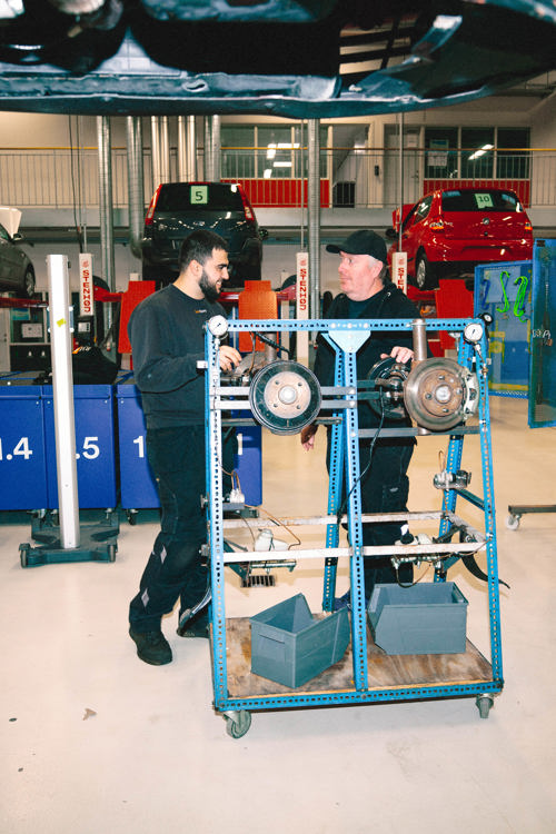 Lærling arbejder med værktøj på en løfteplatform i et værksted, lærling, værktøj, løfteplatform, personvognsmekaniker, værksted, mekanikeruddannelse, bilreparation, erhvervsskole.