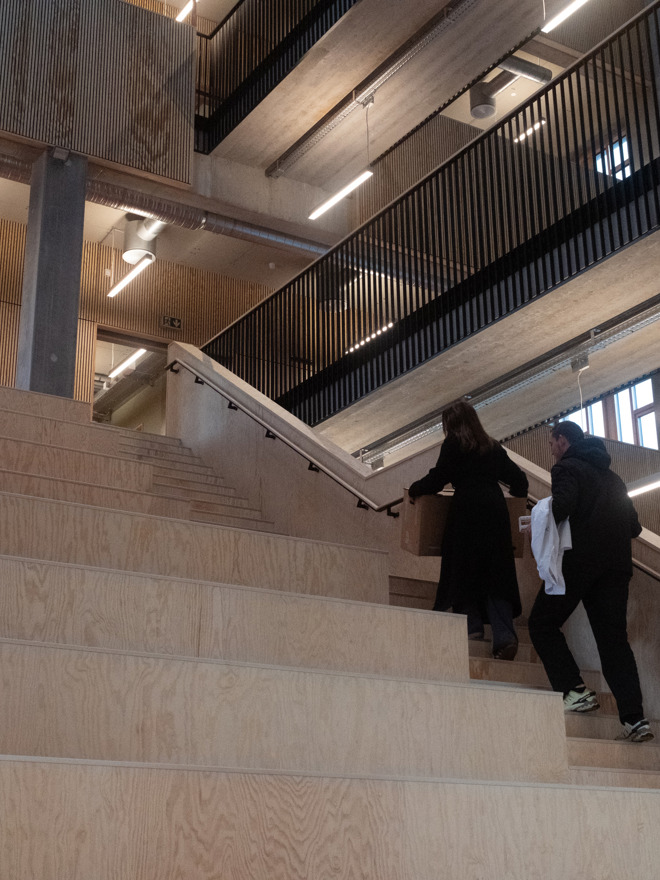 Studerende på TEC går op ad bred trappe i moderne undervisningsbygning med træ og beton – arkitektur og studiehverdag