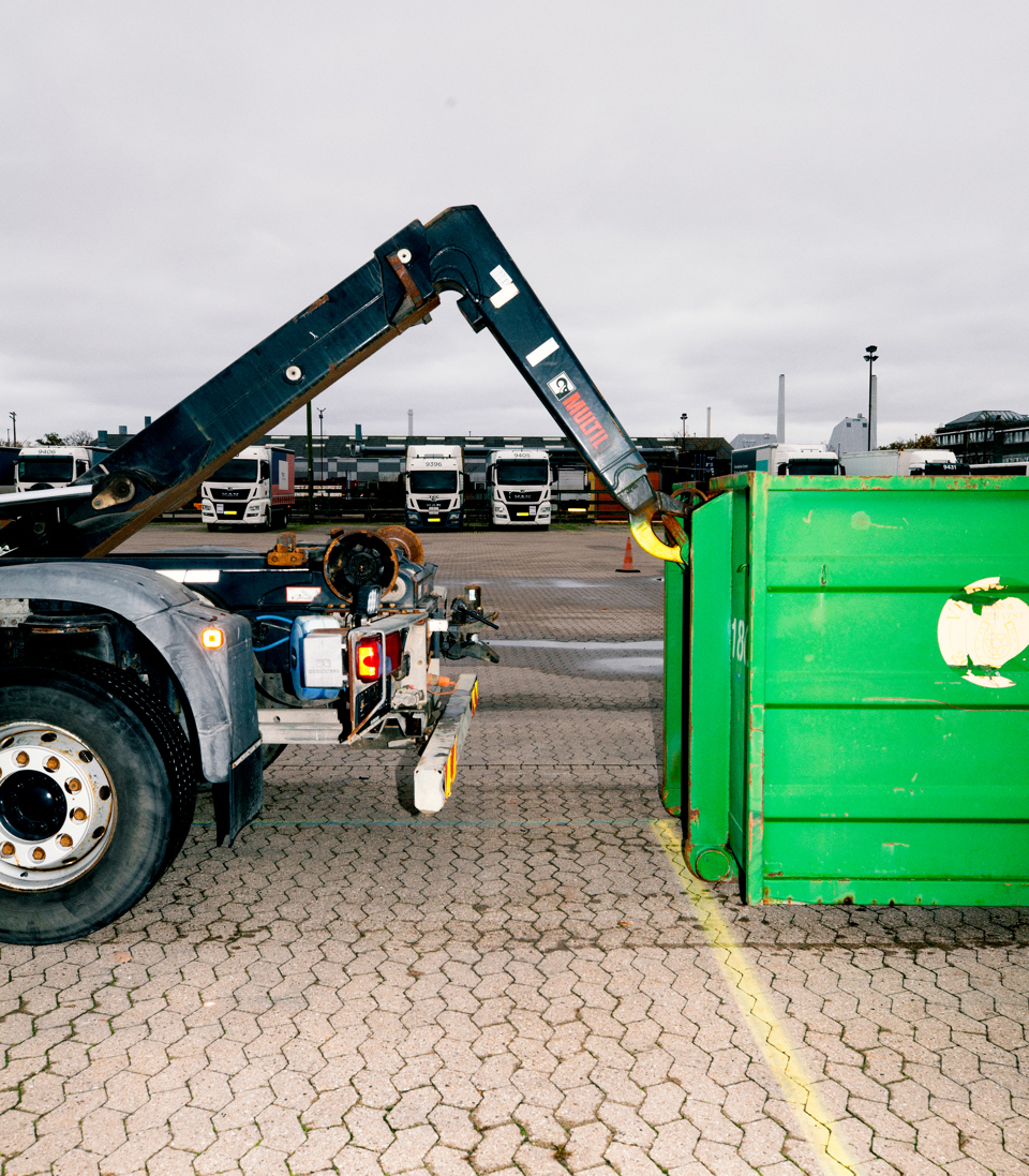 En lastbil med en kranarm er i færd med at påsætte en stor grøn container, chauffør-uddannelsen, chauffør, vejgods, Godshåndtering,  transport,  uddannelsen, vejgodstransport, ContainerLastbil, Kranarm, c