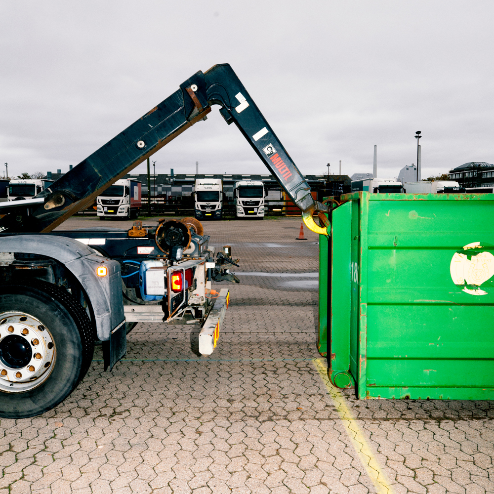 En lastbil med en kranarm er i færd med at påsætte en stor grøn container, chauffør-uddannelsen, chauffør, vejgods, Godshåndtering,  transport,  uddannelsen, vejgodstransport, ContainerLastbil, Kranarm, c