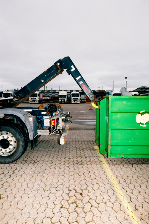En lastbil med en kranarm er i færd med at påsætte en stor grøn container, chauffør-uddannelsen, chauffør, vejgods, Godshåndtering,  transport,  uddannelsen, vejgodstransport, ContainerLastbil, Kranarm, c