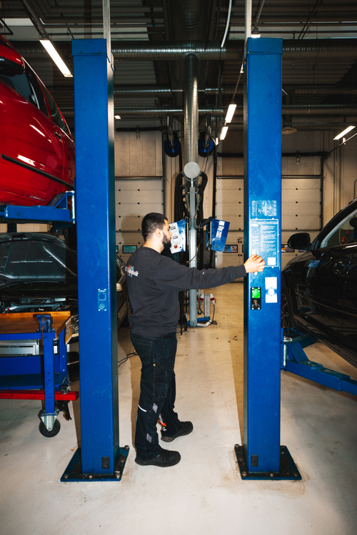 Mekaniker betjener en lift til at hæve en bil i værkstedet, bil, lift, værksted, bilreparation