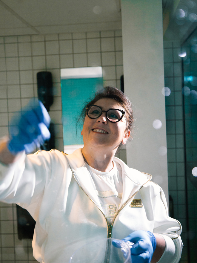 Rengøringstekniker pudser spejl i badeværelse, rengøringstekniker, spejl, pudsning, rengøringsteknikeruddannelsen, badeværelse, rengøringsarbejde, erhvervsskole.